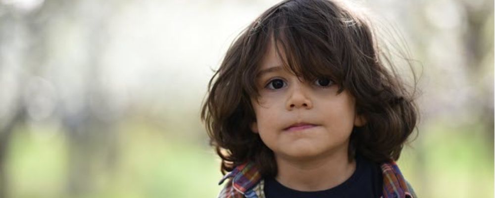 Small child with shoulder length brown hair and brown eyes, biting their lip.